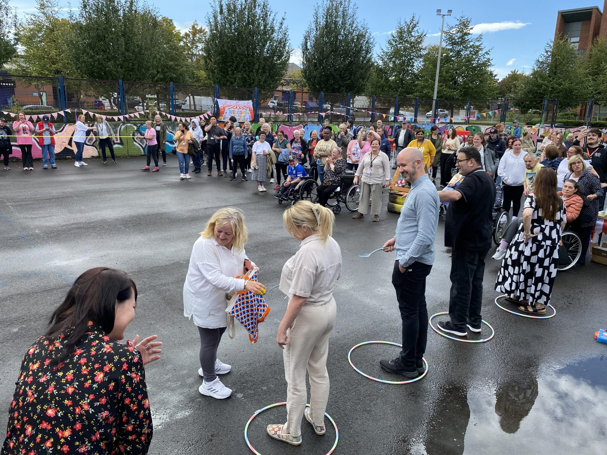 Carr Gomm Glasgow Forum Carr Gomm Glasgow Forum - A row of people are standing holding spoons. A women is giving them eggs from a plastic bag. A group of people can be seen to be watching.