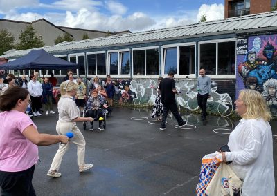Carr Gomm Glasgow Forum - A group of people competing in an egg and spoon race, next to a building with colourful graffiti.