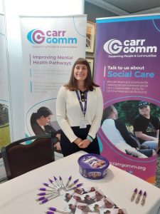 A woman is smiling at the camera. She is surrounded by Carr Gomm pop-up banners and there is a table with sweets and Carr Gomm branded items in front of her at the COSLA conference.