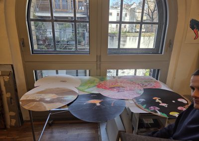 A table full of artwork on big circular paper. The art is based on mushrooms and looks like landscapes.