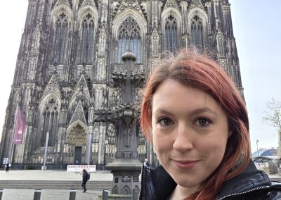 A woman smiles at the camera. Cologne Cathedral can be seen in the background. (EASPD Cologne)