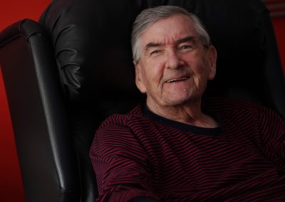 An older man sits in an arm chair smiling.| Carr Gomm Argyll & Bute