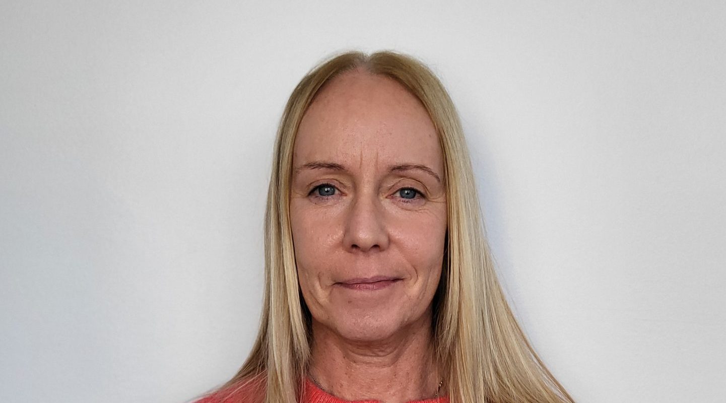 Blonde woman in pink cardigan facing camera