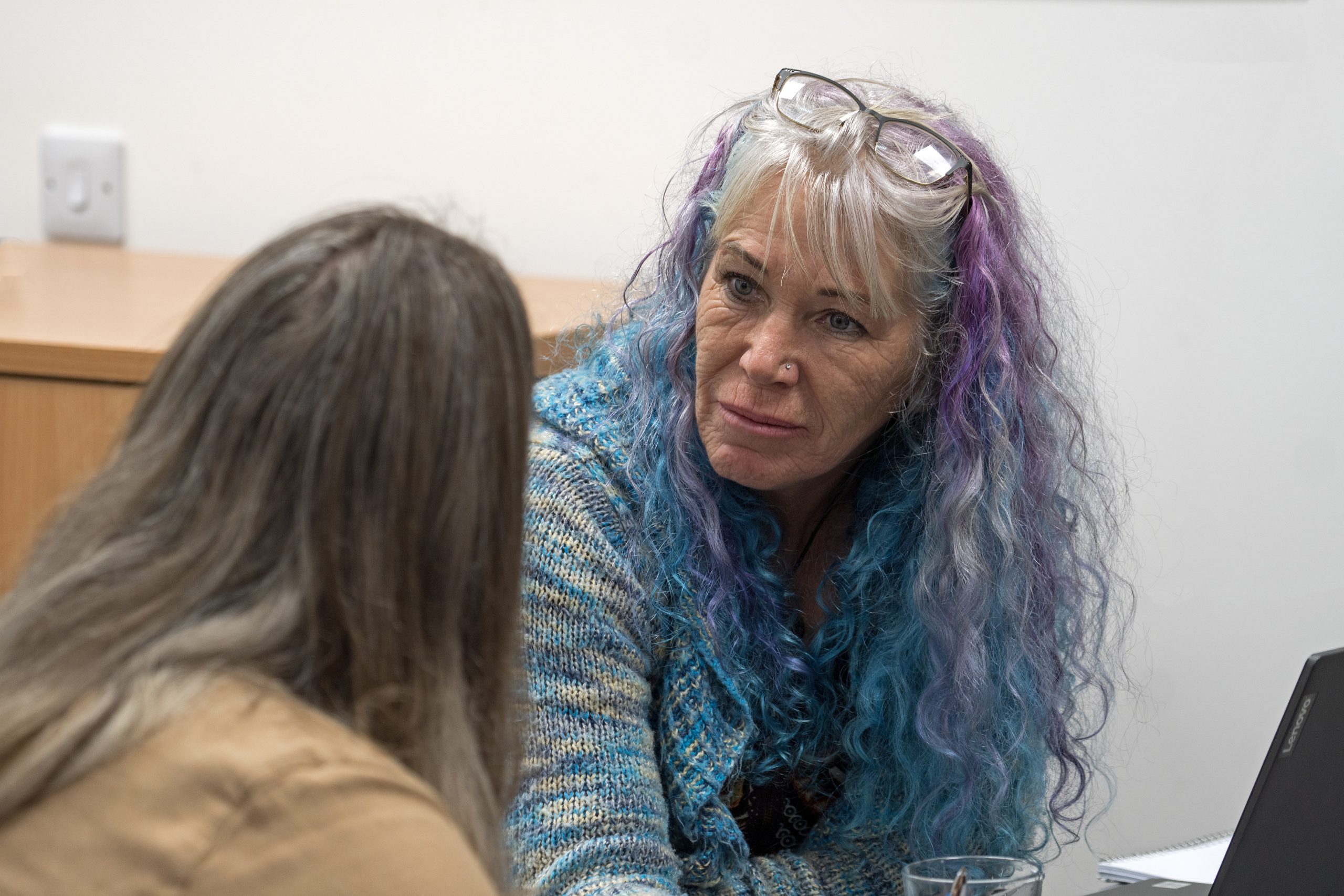 A woman (Jayne) leans forward in deep conversation with another woman whese face is away from the camera. | Carr Gomm Mental Health Support