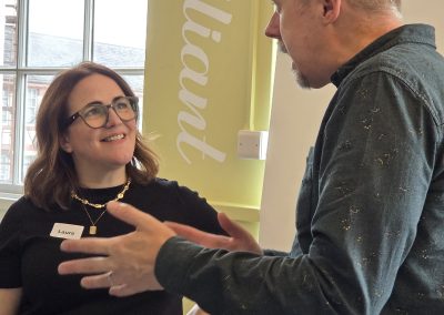 Man with grey hair speaking to woman with glasses