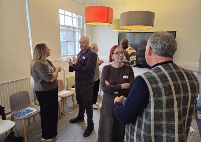 6 people in a room, speaking to each other in groups of two and three.