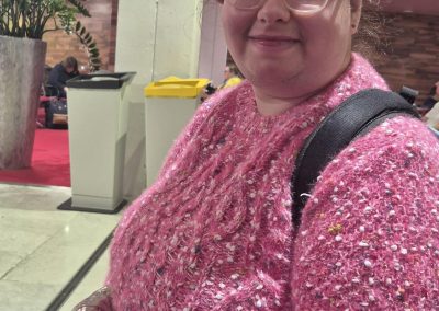 A woman (Edina) wearing a pink sweater and a pink beret sits in a hotel lobby