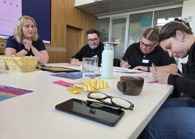4 people sat at a table writing on small pieces of paper.