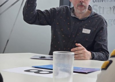 Man in dark patterned shirt sitting at a table with hand raised in the air.