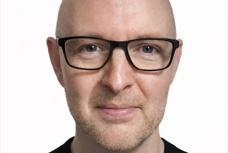 Bald man with dark rimmed glasses and dark top.