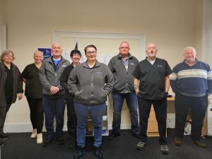 8 men and women standing in an office setting and smiling