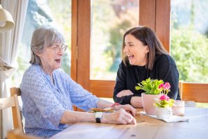 Two women sitting at a table in a conservatory laughing.