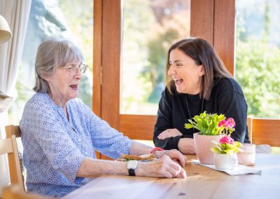 Two women sitting at a table in a conservatory laughing.