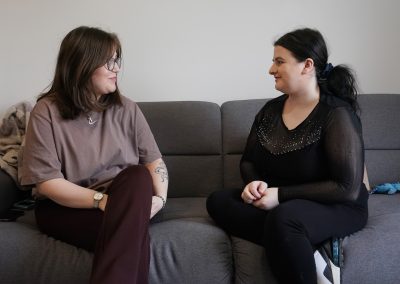 Two young women sit facing each other on a sofa. One is a Support Practitioner.