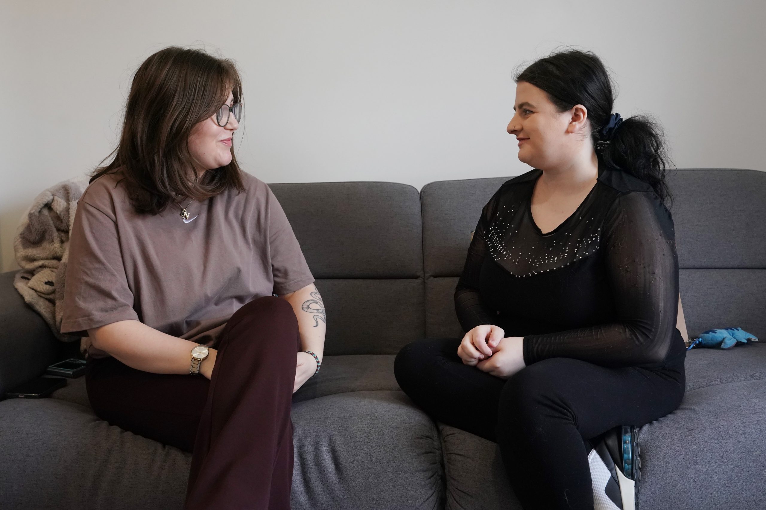 Two young women sit facing each other on a sofa