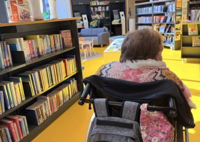 A woman who is a wheelchair user sits with her back to the camera in a vibrant library