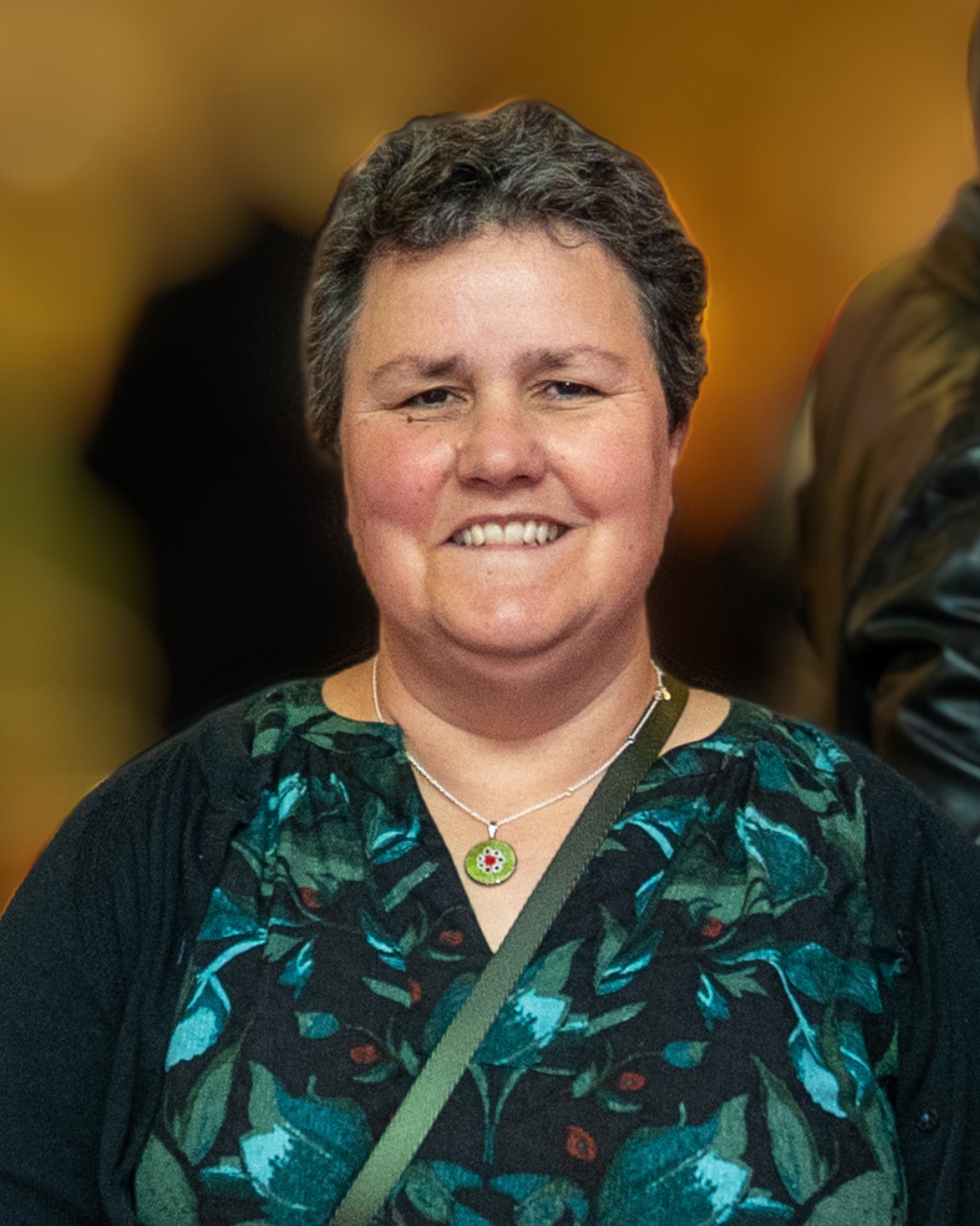 Becs Barker Carr Gomm A woman with short dark hair wearing a patterned dress and cardigan against a softly blurred background