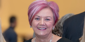 A woman (Mandy Hay) with pink highlights wearing a diamond necklace against a soft blurred background.