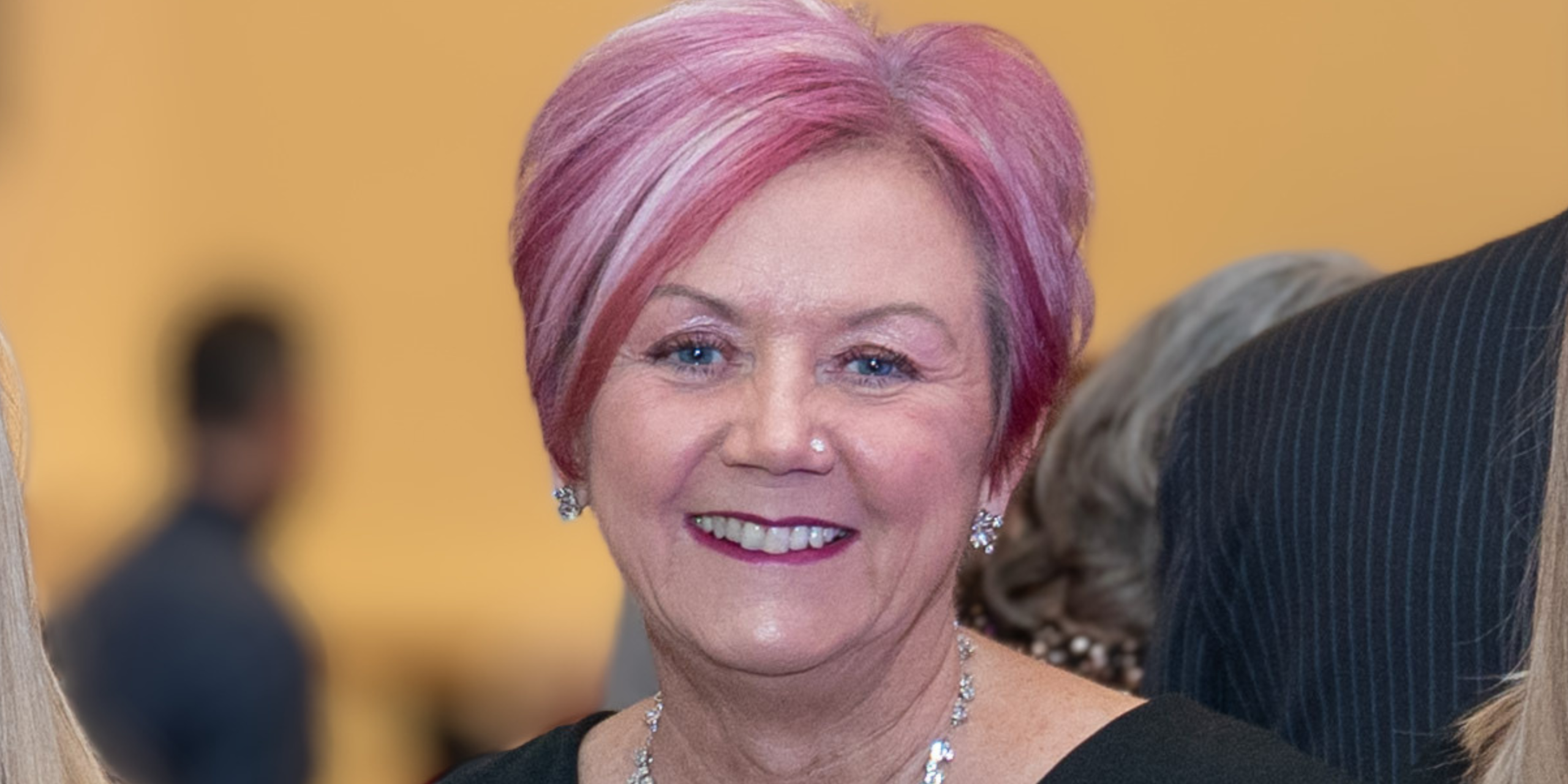 A woman (Mandy Hay) with pink highlights wearing a diamond necklace against a soft blurred background.