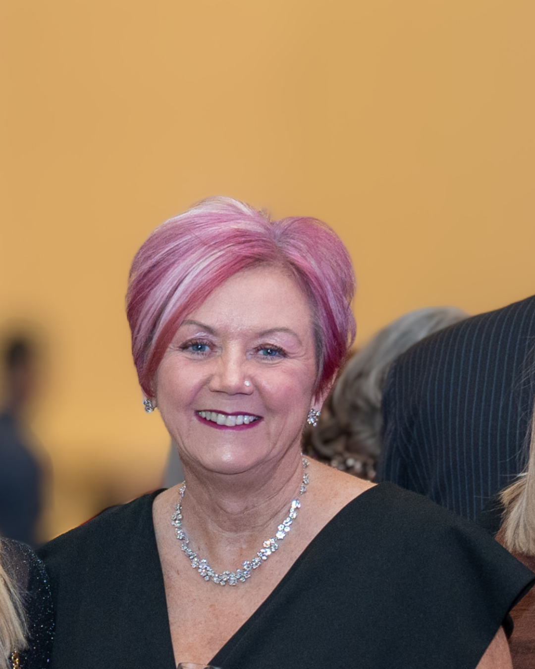 A woman (Mandy Hay) with pink highlights wearing a diamond necklace against a soft blurred background.
