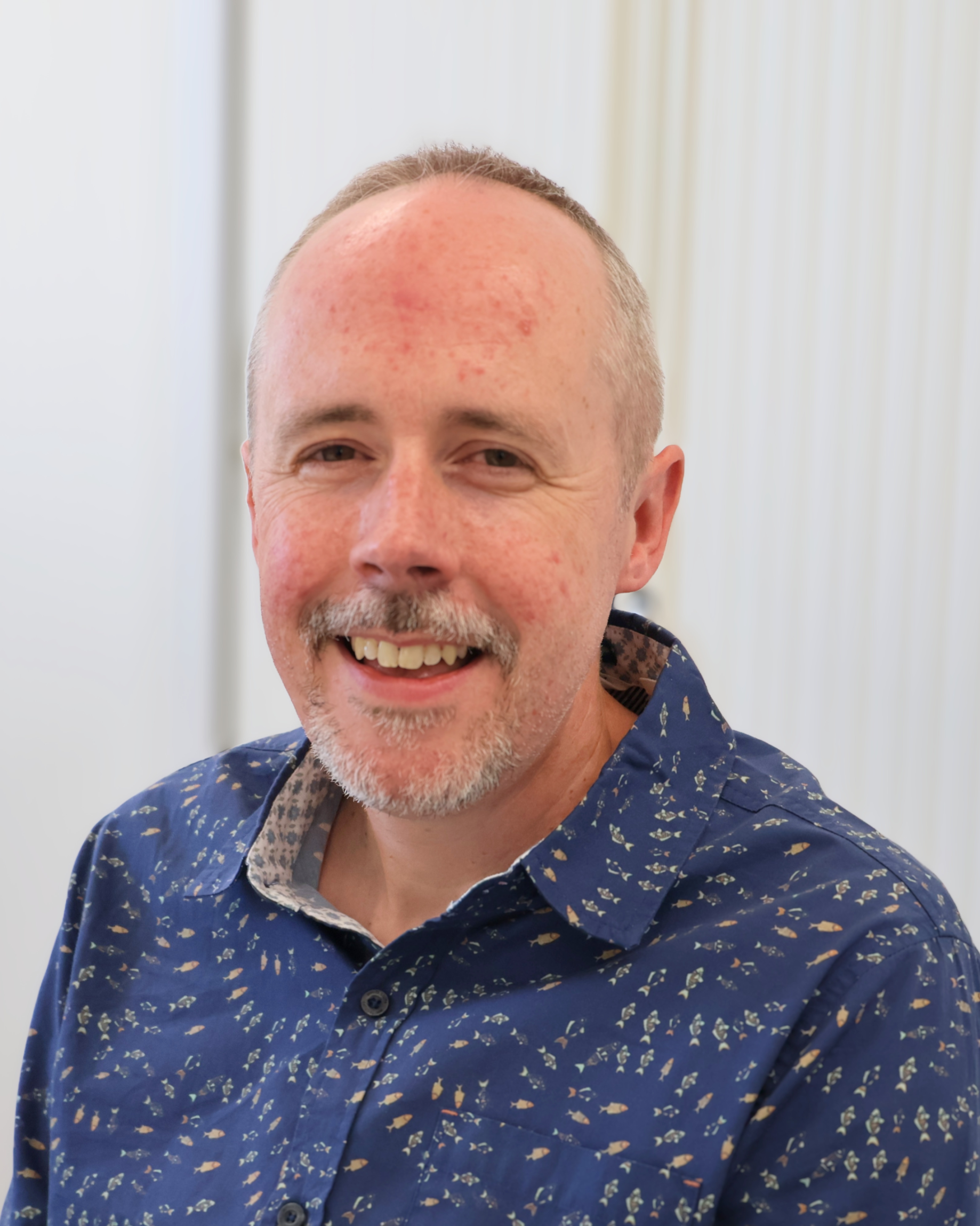 A man (Paul Marshall) with a short beard and a blue patterned shirt smiles at the camera. | Carr Gomm