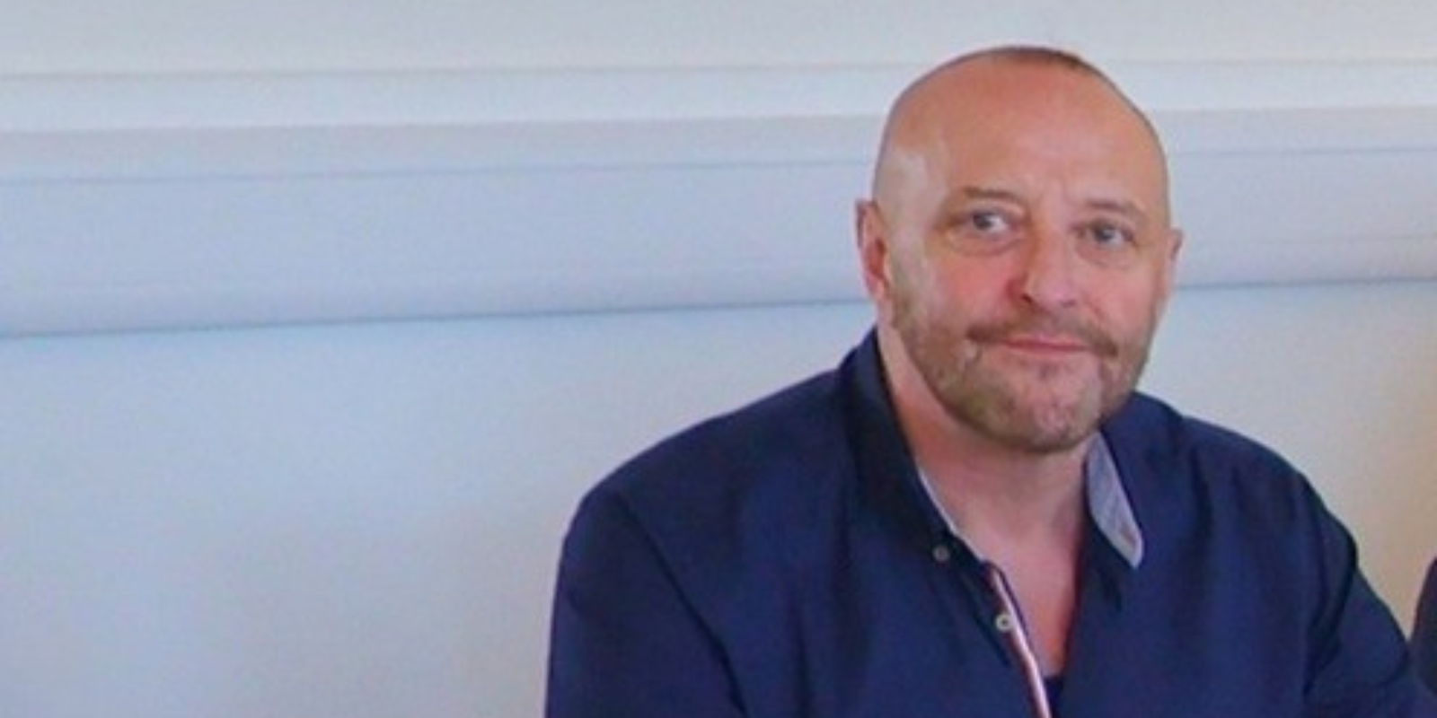 A man (Craig Sutherland) wearing a suit with a deep purple tie.