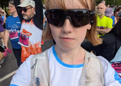 A young woman wearing sunglasses, a Carr Gomm tshirt and running vest. In the background are other runners.