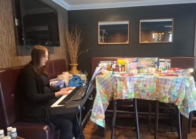 A woman plays the keyboard. In the background is a table decorated and displaying raffle prizes