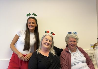 Three women sitting on a sofa wearing decorative flags in their hair. On the wall behind them are flags from around the world.