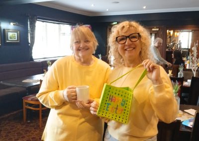 Two women wearing yellow tops pose for a picture in a restaurant environment.