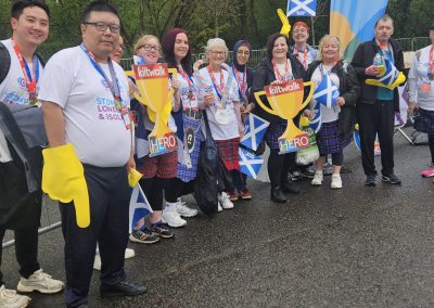 A group of people wearing Carr Gomm tshirts pose for a picture holding Scotland flag and trophy cut outs.