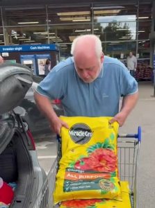 A man (Ant) adding two bags of yellow compost to a trolley.