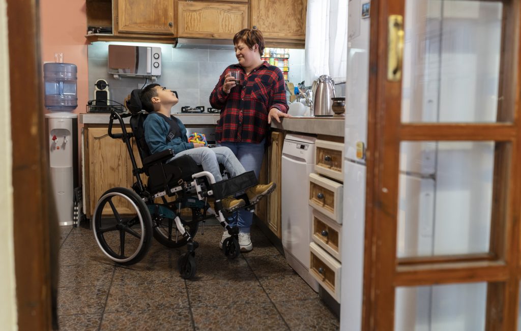 A woman drinking coffee in the kitchen with a boy who uses a wheelchair. | Carr Gomm Children's Services