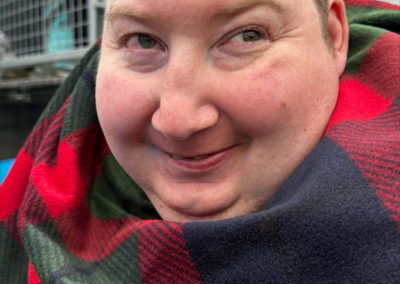 A man smiles at the camera while wrapped in a red tartan scarf