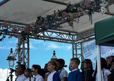 A group of school children are performing on an outdoor stage in the sunshine